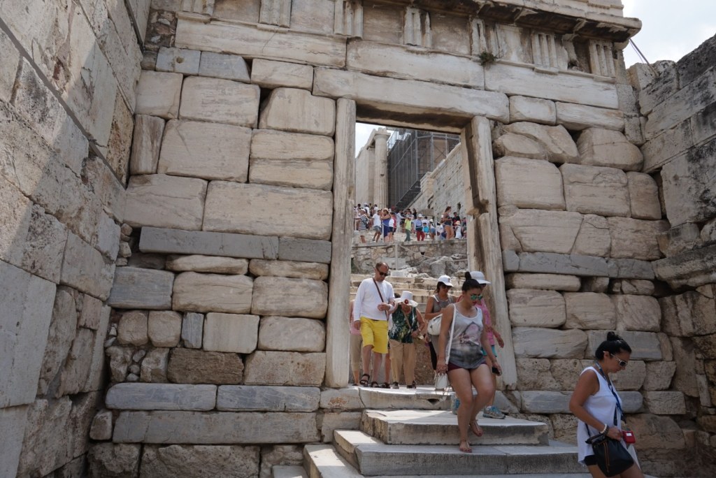 A monumental doorway through the Propylaea, visitors coming down the marble steps and more queueing beyond