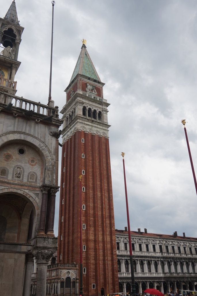 The brick campanile of St Mark's above the Piazzetta, flagpoles and an arcaded building beside it