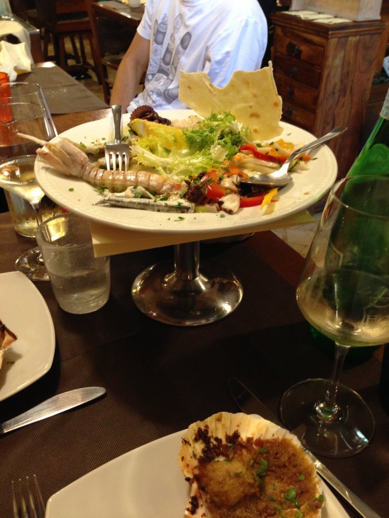 A seafood antipasto on a raised stand, prawns and marinated vegetables with a crisp wafer and a glass of white wine