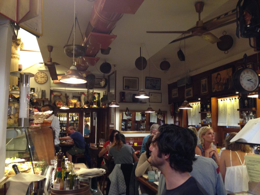 The interior of a busy Venetian bacaro, copper pans hung beneath a white barrel ceiling and every table full