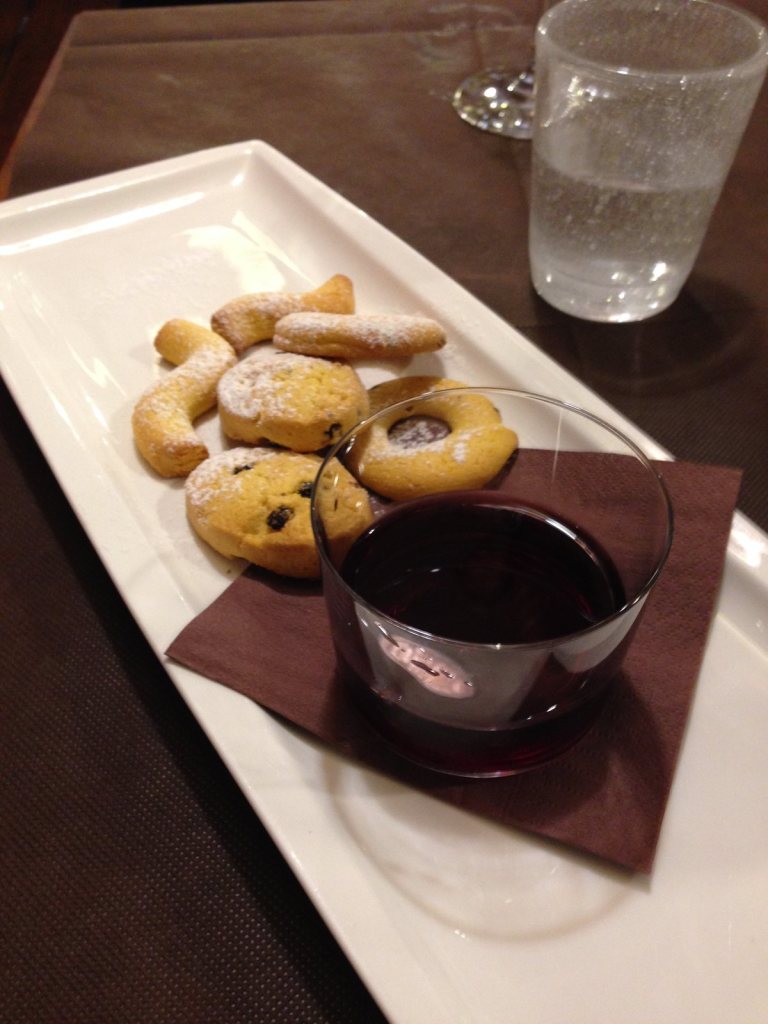 Small sugared biscuits on a plate beside a glass of dark red wine