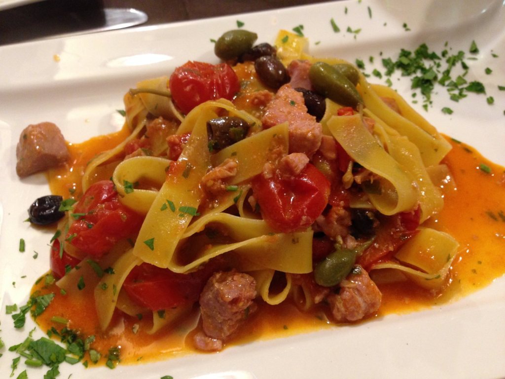 Wide ribbon pasta in a tomato sauce with green and black olives and chopped herbs