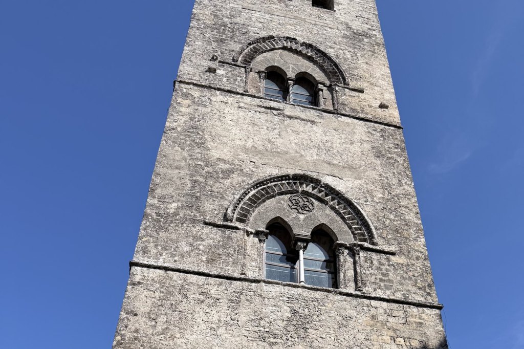 The freestanding stone bell tower of the Chiesa Madre in Erice, Sicily, against a deep blue sky.