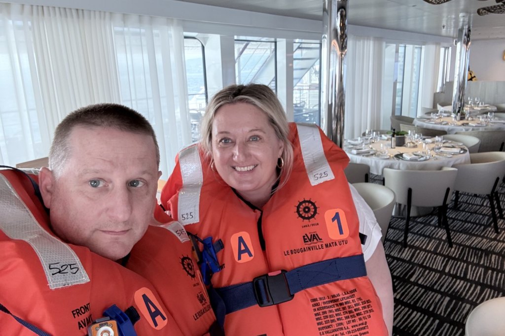 Chris and Jen Moss wearing orange life jackets in the dining room of Le Bougainville during the safety drill.