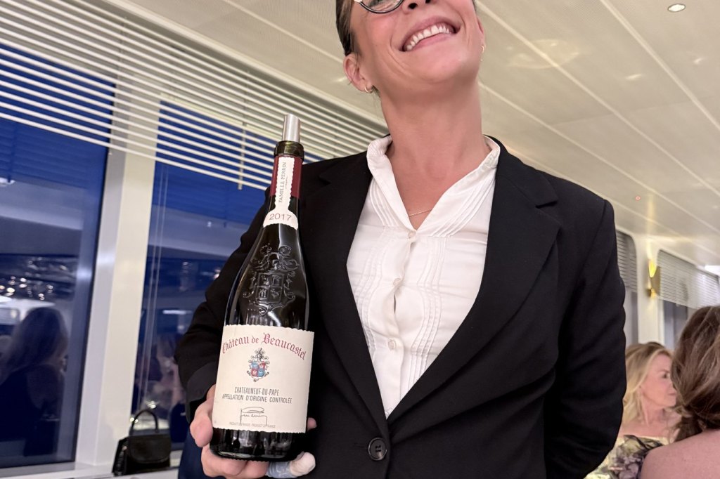 A smiling sommelier presenting a bottle of 2017 Château de Beaucastel Châteauneuf-du-Pape in the ship’s restaurant.