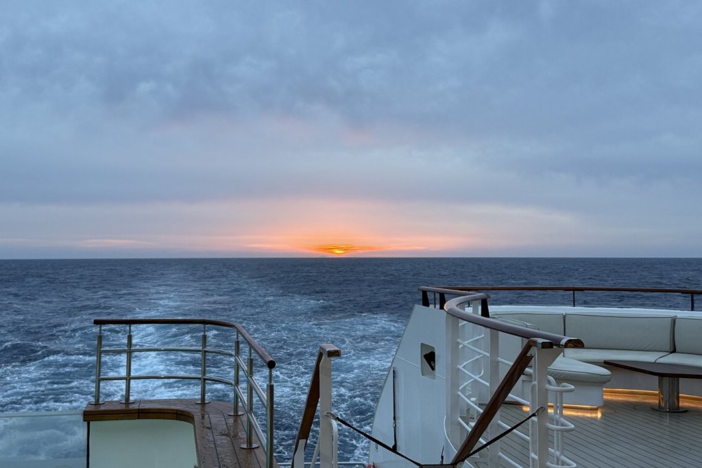 The sun setting through a band of storm cloud over open water, seen from the stern deck of Le Bougainville.