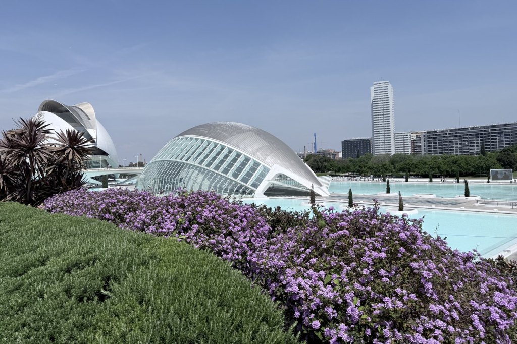 The eye-shaped dome of L’Hemisfèric at Valencia’s City of Arts and Sciences, reflected in a turquoise pool behind purple flowers.