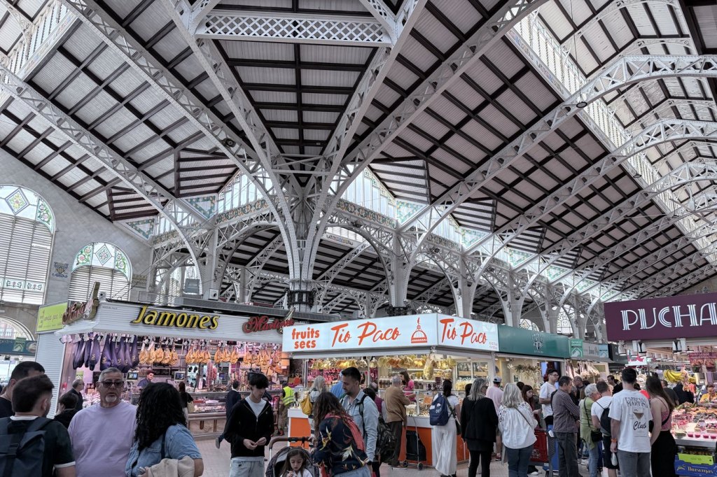 The iron and glass interior of Valencia’s Mercado Central, crowded with shoppers moving between the stalls.