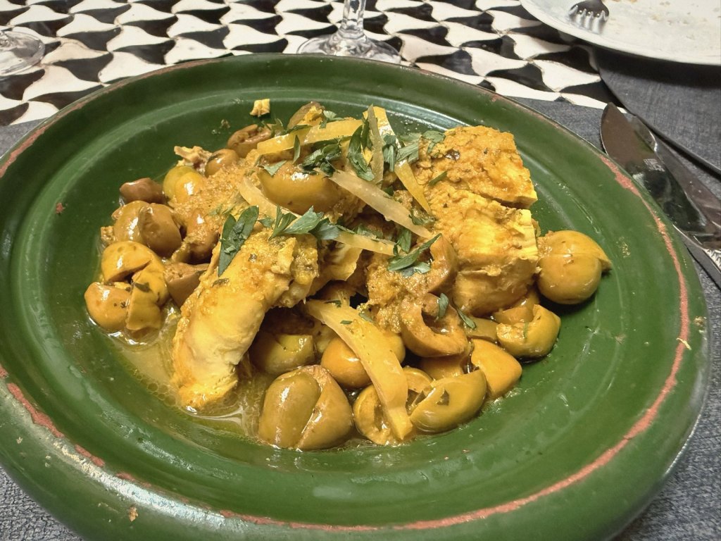 Chicken tagine with green olives and strips of preserved lemon, scattered with parsley, in a green glazed earthenware dish