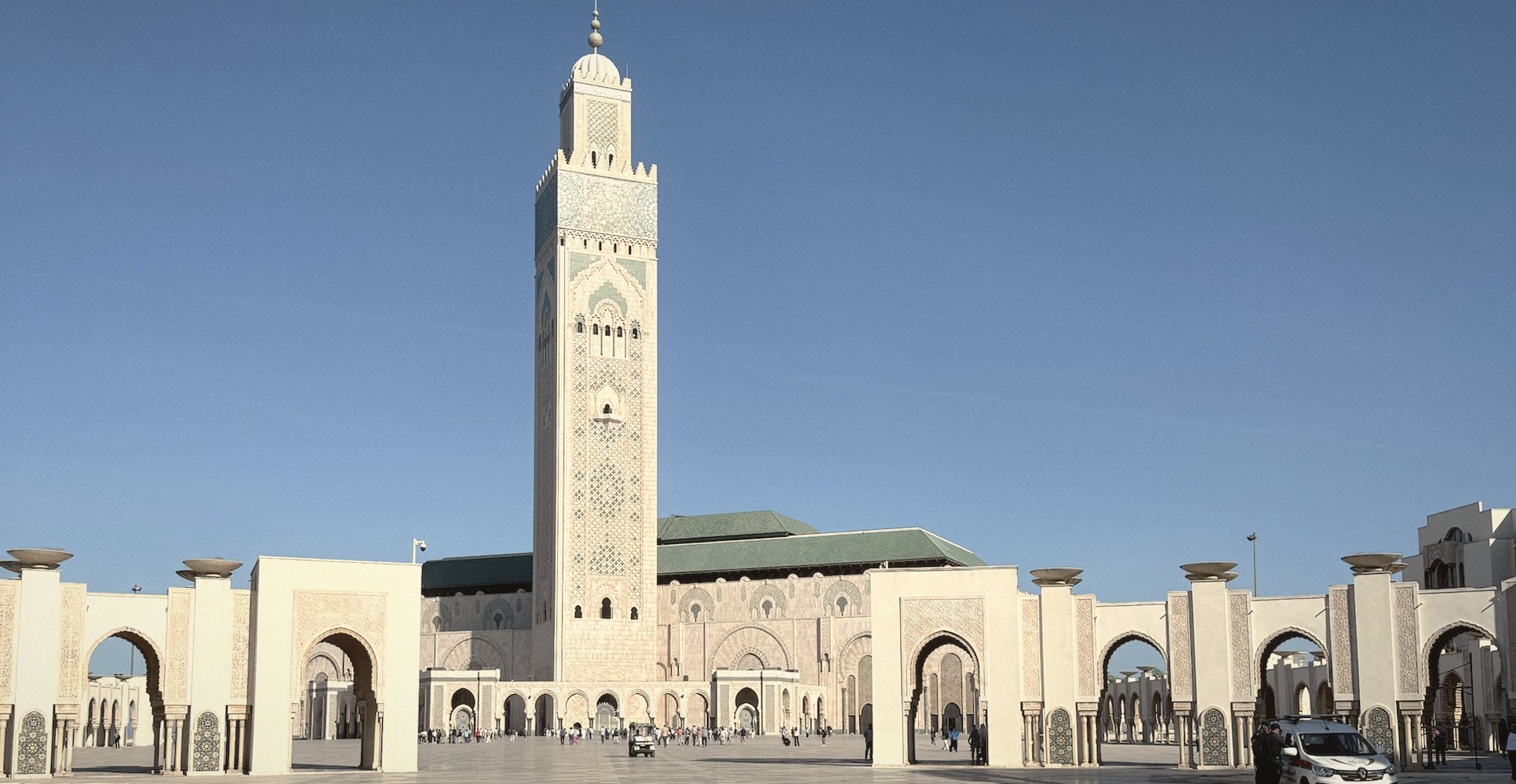 The minaret of the Hassan II Mosque rising above the arcades at the edge of its vast marble esplanade, under a deep blue sky
