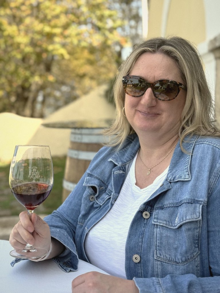 Jen at the tasting table in sunglasses, holding up a glass of red wine etched with the Casal Sta. Maria crest