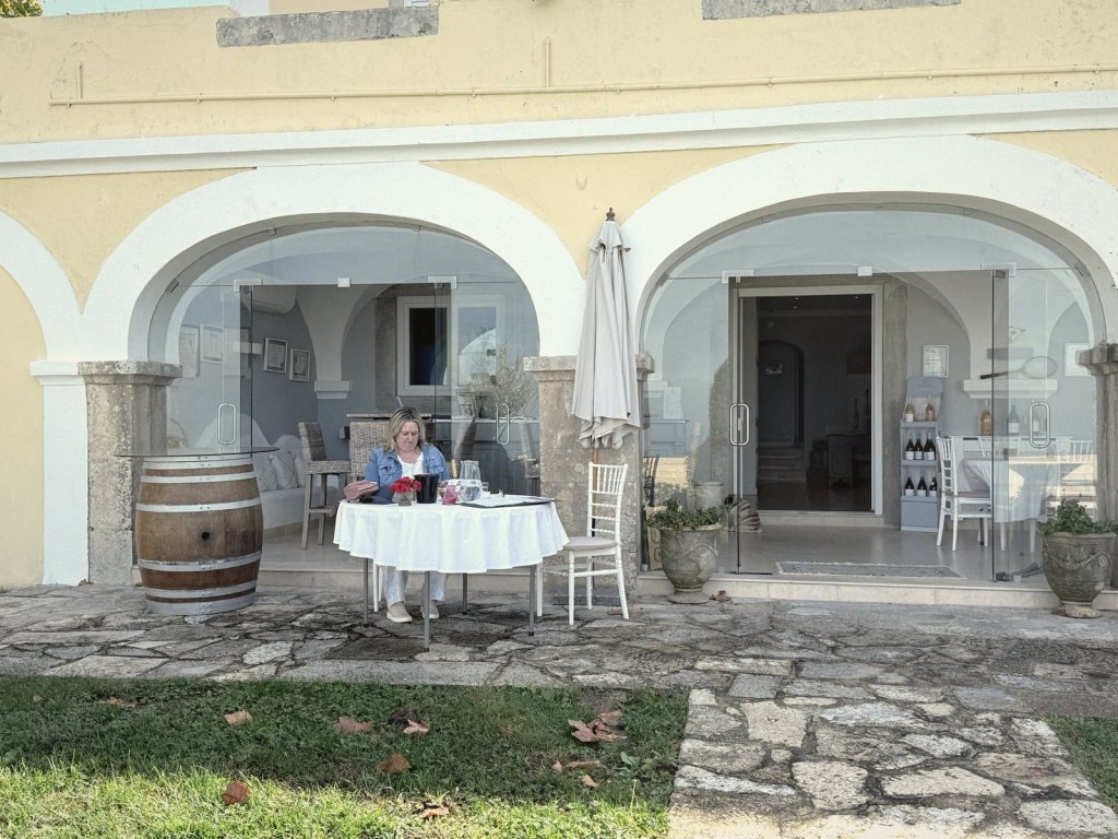 Two whitewashed stone arches of the tasting room, with a round table under a white cloth set up outside them and a wine barrel standing alongside